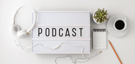 Podcast word on lightbox with headphones, notepad and coffee cup, podcast concept, flat layの写真素材