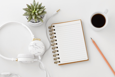 Headphones with notebook, pencil, coffee cup on white deskの写真素材
