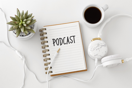 Podcast word on notebook with headphones and coffee cup on white desk, flat layの写真素材