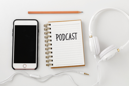 Podcast word on notebook with smartphone and headphones on white desk, top viewの写真素材