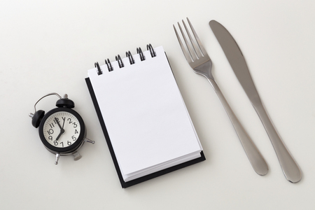 Clock and notepad with fork and knife, intermittent fasting and weight loss plan conceptの写真素材
