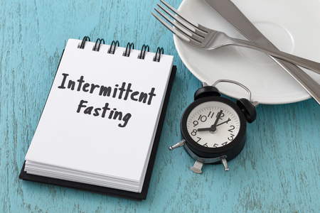Intermittent fasting word on notepad with clock, fork and knife on white plate, intermittent fasting and weight loss  conceptの写真素材