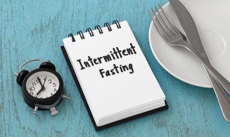 Intermittent fasting word on notepad with clock, fork and knife on white plate, weight loss and diet conceptの写真素材