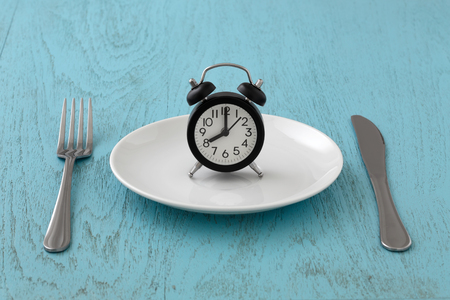 Clock on white plate with fork and knife, intermittent fasting, meal plan, weight loss concept on blue tableの写真素材