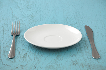 White plate with fork and knife on blue tableの写真素材