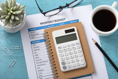 Monthly budget concept with white calculator and coffee cup on blue wooden tableの写真素材