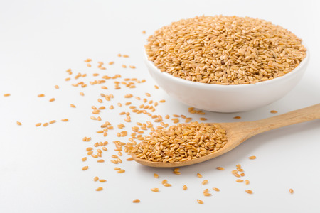 Golden flaxseed in wooden spoon and bowl on white background with spaceの写真素材