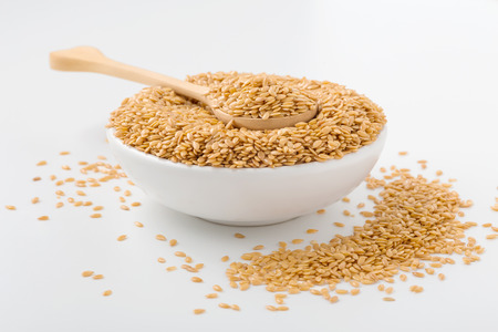 Golden flaxseed in wooden spoon and bowl on white backgroundの写真素材