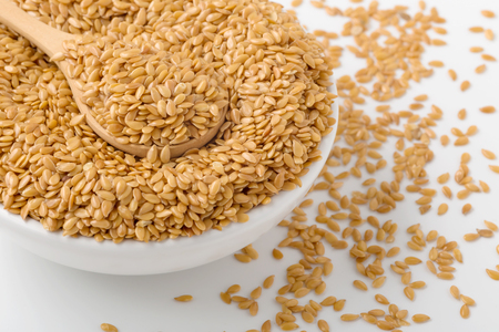 Golden flaxseed in wooden spoon and bowl on white background, closed upの写真素材