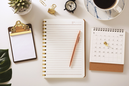 Flat lay desk with notebook, calendar, clipboard and pen, golden accessories, warm toneの写真素材
