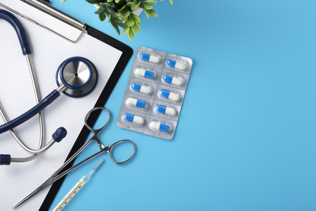 Doctor desk with pills and stethoscope, top view, blue backgroundの写真素材