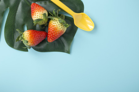 Strawberries on green leaf with yellow spoon on light blue background, flat layの写真素材
