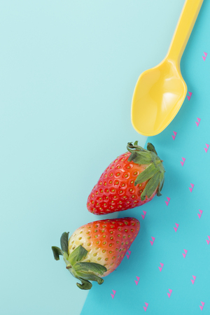 Strawberries with yellow spoon on two tone blue background, flat layの写真素材