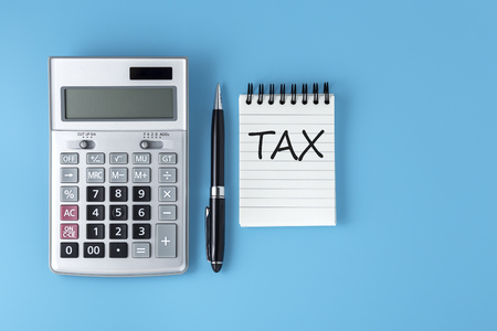 Tax word on notepad with calculator and pen on light blue background, flat layの写真素材