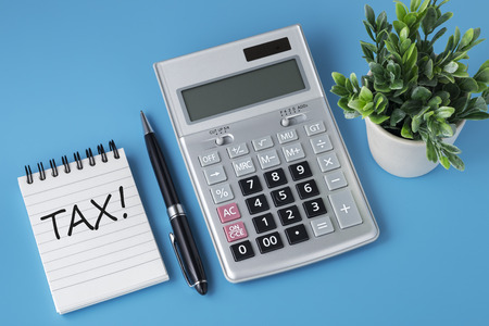 Tax word on notepad with calculator and pen on blue backgroundの写真素材