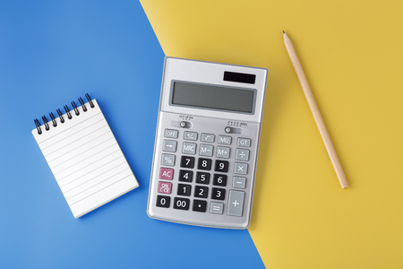 Sliver calculator on yellow and blue background with notepad and pencil, flat lay with spaceの写真素材