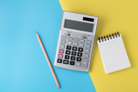 Calculator on light blue and yellow background with notepad and pencil, flat lay with spaceの写真素材