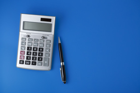Sliver calculator on blue background with black pen, flat lay with spaceの写真素材