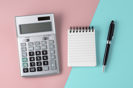 Calculator on pastel pink and blue background with notepad and pen, flat layの写真素材