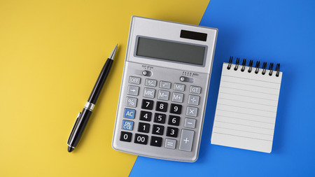 Calculator on vivid yellow and blue background with black pen and notepad, flat lay with spaceの写真素材