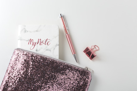 Glitter bag with pen, planner notebook, pink gold accessories on white desk, flat layの写真素材