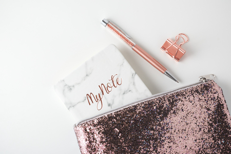 Glitter bag with pen, planner notebook, pink gold accessories on white desk backgroundの写真素材