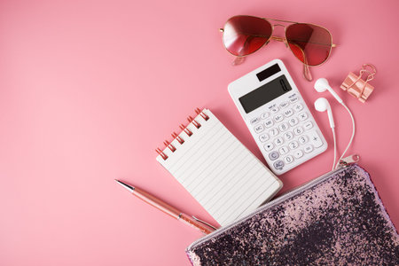 Fashion glitter bag with note pad, calculator and sunglasses on pink background