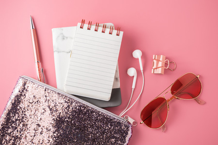 Fashion glitter bag with note pad, sunglasses, earphone and pen on pink backgroundの写真素材