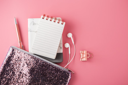 Fashion glitter bag with note pad, earphone and pen on pink background, flat layの写真素材