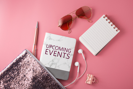 Upcoming events book with fashion glitter bag, sunglasses, earphone and pen on pink backgroundの写真素材