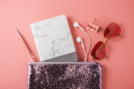 Fashion glitter bag with marble notebook, earphone, sunglasses and pen on coral pink backgroundの写真素材