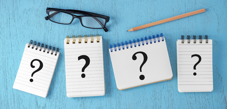 Question marks on notepads on blue wooden desk, variety of questions, faq concept, top viewの写真素材