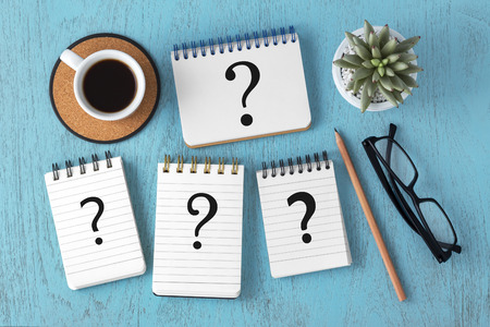 Question marks on notepads on blue wooden table with coffee cup, faq concept, top viewの写真素材