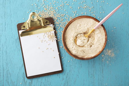 Quinoa flour in bowl with clipboard and quinoa seeds on blue wooden tableの写真素材