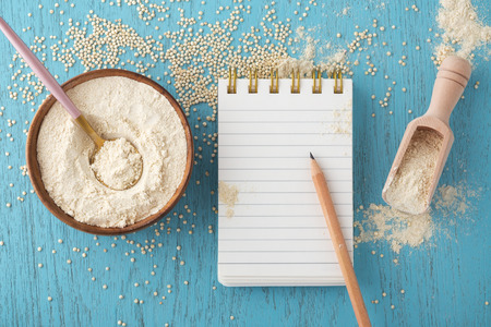 Quinoa flour in bowl with notepad and pencil on blue wooden table, gluten free bakingの写真素材