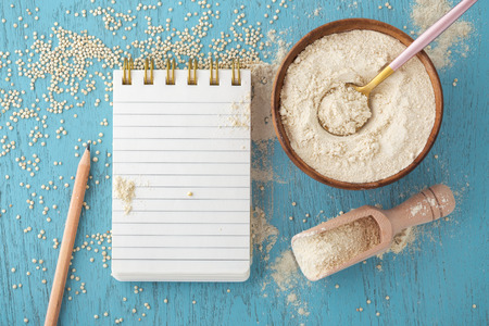 Quinoa flour in bowl, notepad and pencil with quinoa seeds on blue wooden table, top viewの写真素材