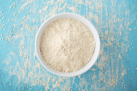 Quinoa flour in white bowl with quinoa seeds on blue wooden table, top viewの写真素材