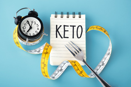 Keto word on notebook with clock fork and measuring tape around on blue background, intermittent fasting on keto conceptの写真素材