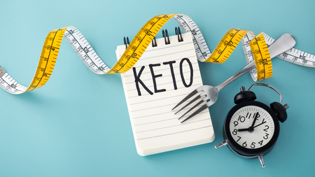 Keto word with clock, fork and measuring tape around on blue background with spaceの写真素材