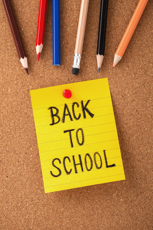 Back to school on yellow note with color pencils on cork board background, top viewの写真素材