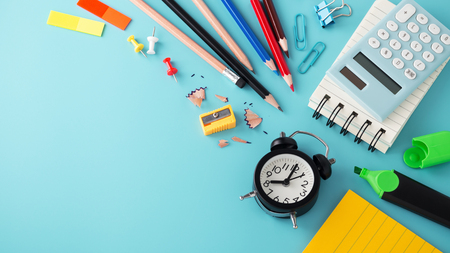 School stationery with clock on blue background with copy space, back to school conceptの写真素材