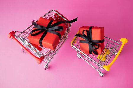 Red gift box with black bow in shopping carts on pink backgroundの写真素材