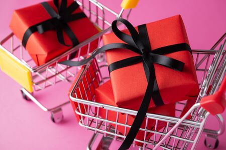 Red gift box with black bow closeup in shopping cart on pink backgroundの写真素材
