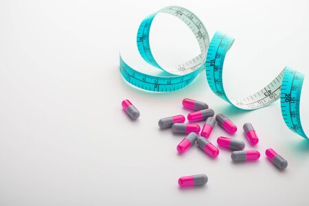 Diet supplements, pills, pink capsule with blue measuring tape, diet and weight loss conceptの写真素材