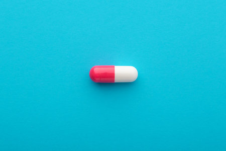 Pharmaceutical pill, pink white capsule on blue background, flatlay