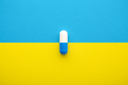 Medical pill, blue white capsule on yellow background, top view