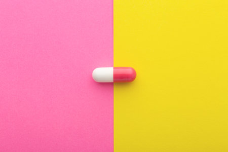 Pharmaceutical pill, pink white capsule on yellow background, top view