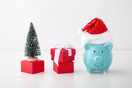 Piggy bank wearing christmas hat with red gift box and christmas tree on white backgroundの写真素材