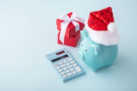 Piggy bank wearing christmas hat with red gift box and calculator on pastel blue backgroundの写真素材