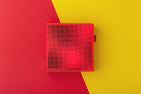 Red wireless speaker on red and yellow background, flat lay